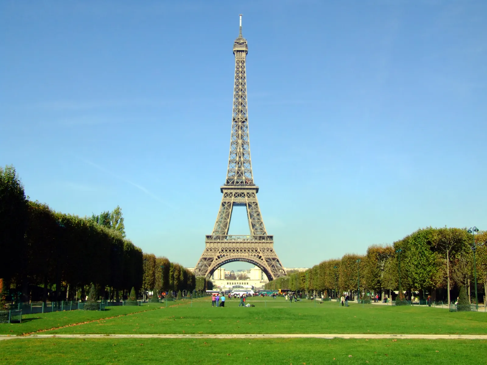 The Eiffel Tower viewed from the tree-lined lawn of Champ de Mars park on a clear day
