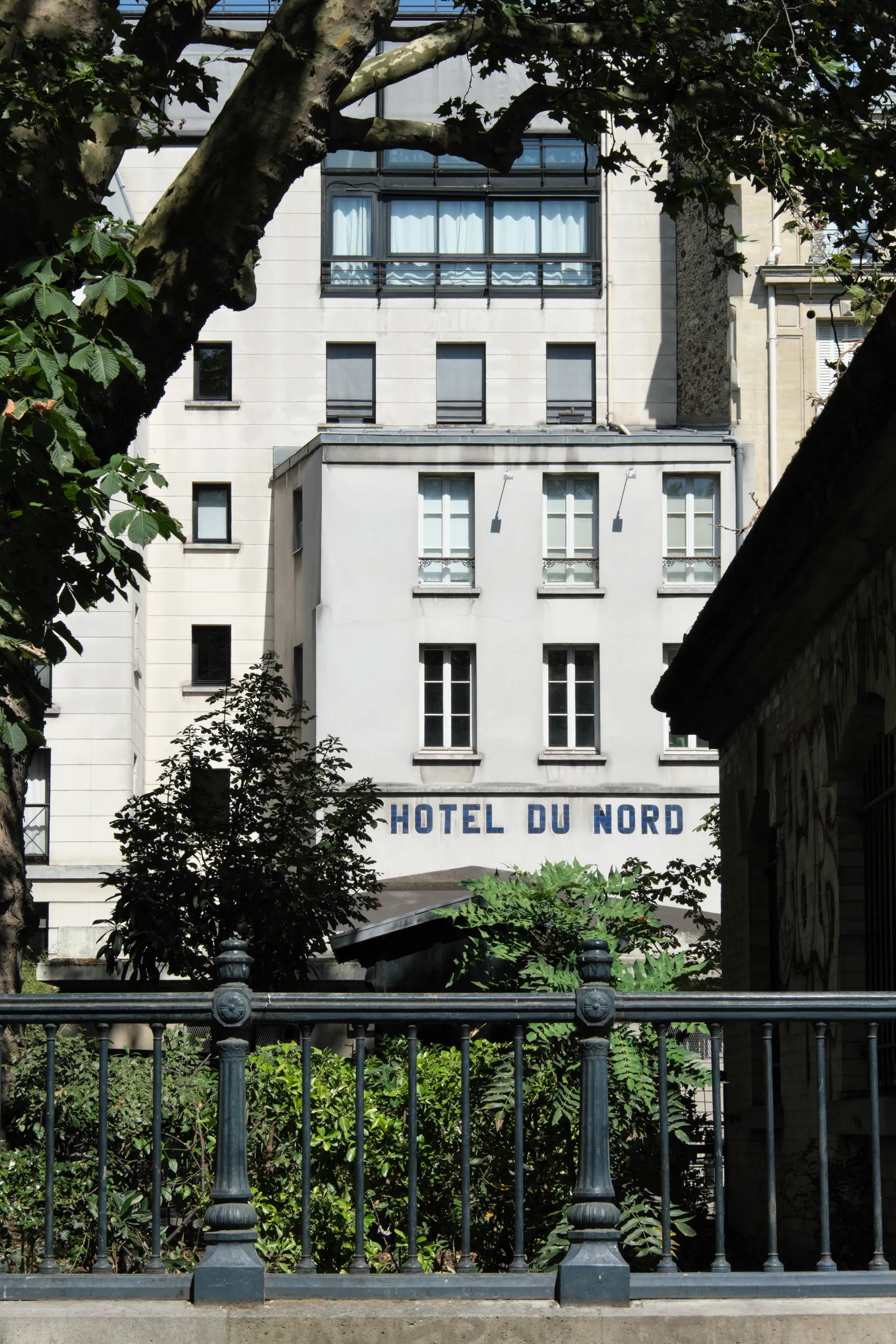 The white facade of the Hôtel du Nord on the Quai de Jemmapes in Paris, with its blue painted lettering across the front, seen from the canal path through plane trees