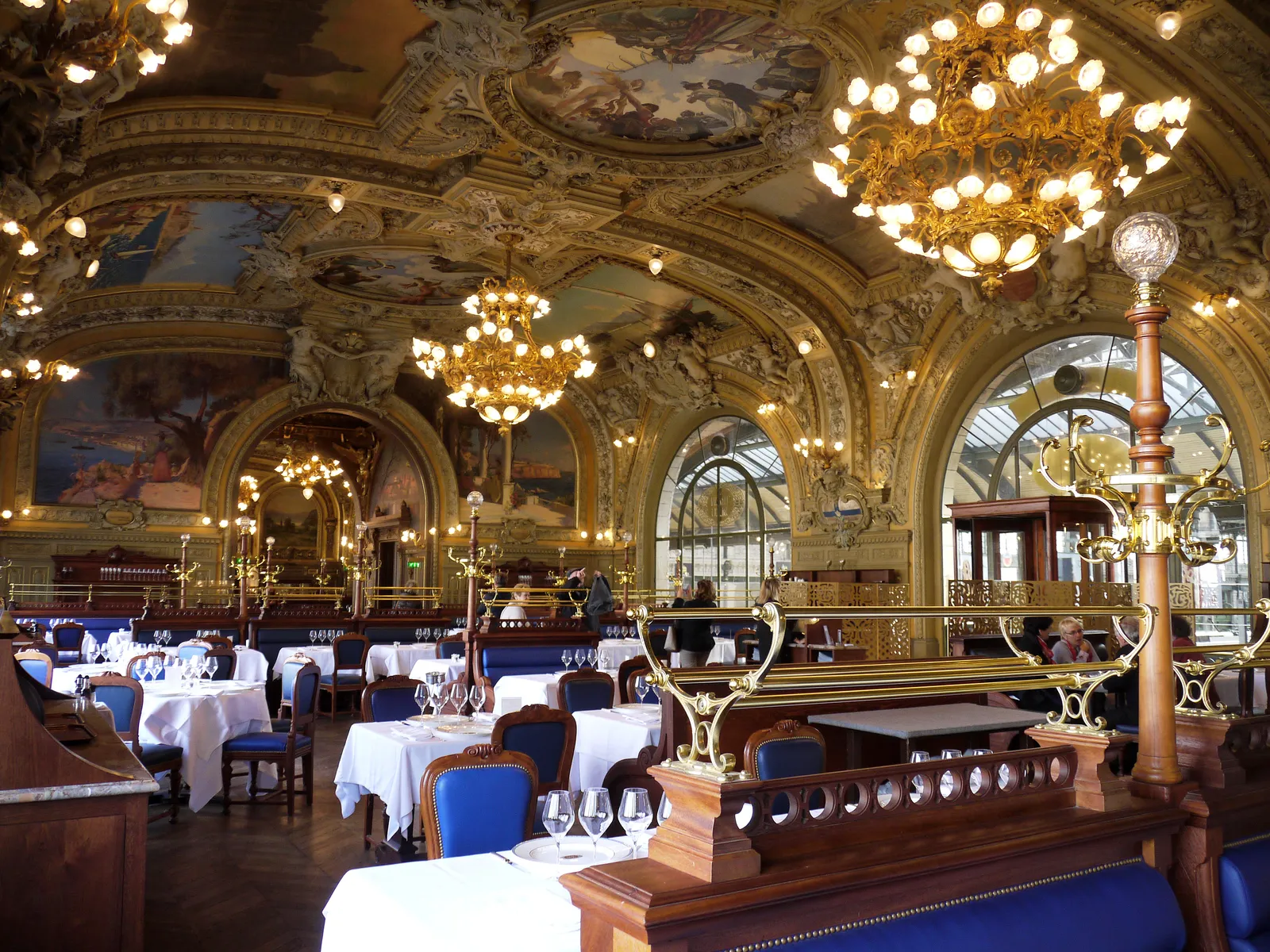 The dining room of Le Train Bleu above Paris Gare de Lyon, its vaulted ceiling covered in painted panels and gilt plasterwork, with chandeliers over rows of set tables