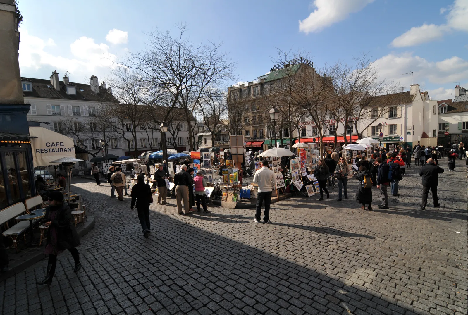 Artists displaying paintings for sale on the cobbled Place du Tertre in Montmartre, with cafes lining the square