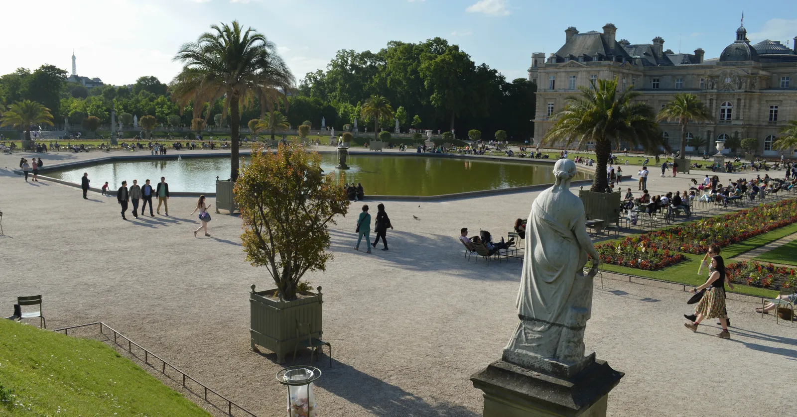 The Grand Bassin in the Jardin du Luxembourg in Paris on a summer afternoon, with the Luxembourg Palace behind it and people sitting in green metal chairs around the gravel terraces