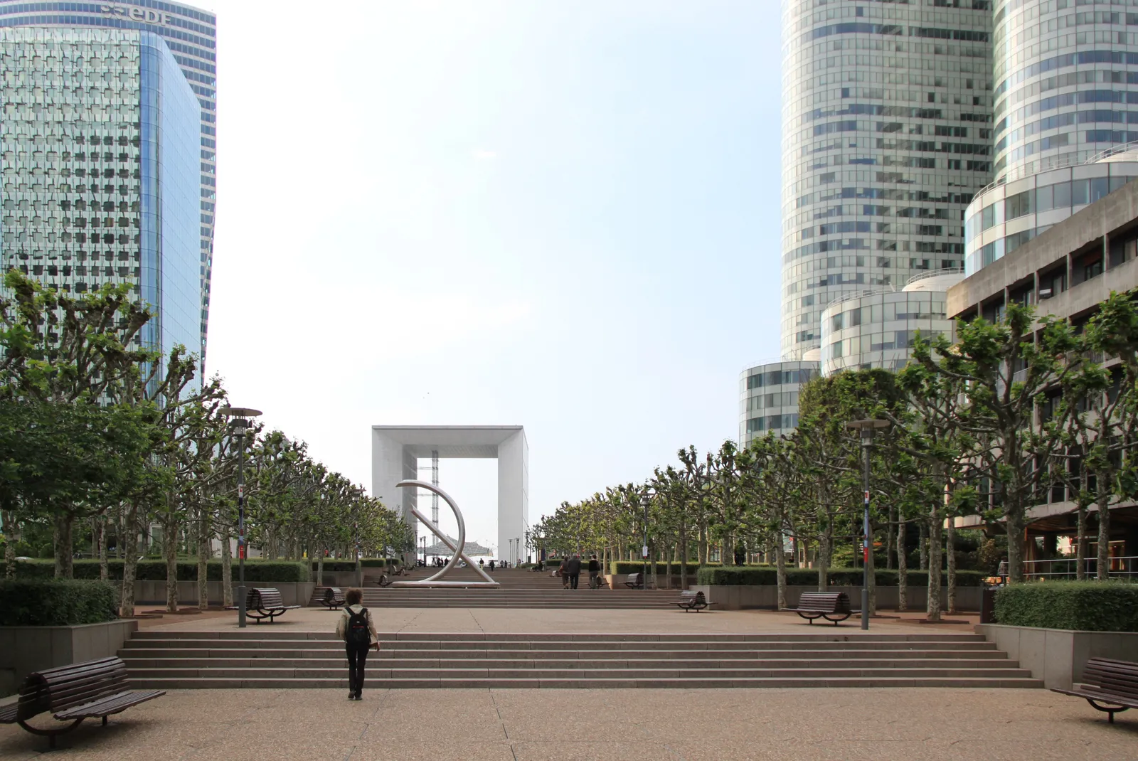 The Grande Arche at La Défense framed by glass skyscrapers along a tree-lined pedestrian esplanade