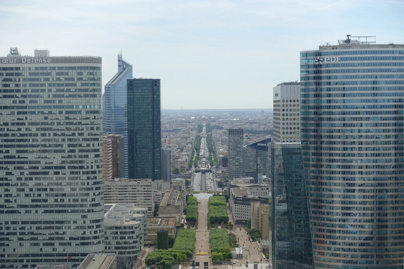Looking east along the Paris historic axis from the Grande Arche at La Défense, the line running dead straight between office towers to the Arc de Triomphe in the distance
