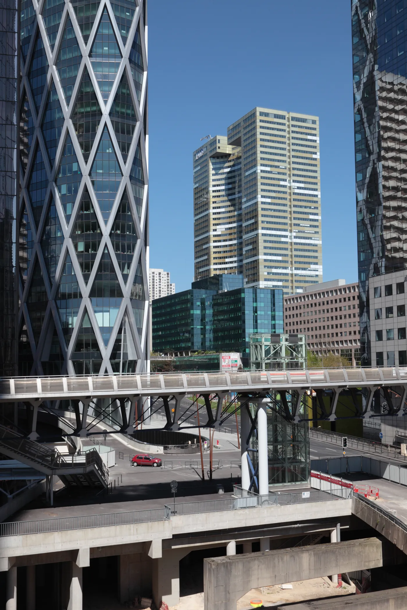 Glass towers at La Défense in Paris above a raised pedestrian deck, with a footbridge crossing over the roads and service ramps running underneath it