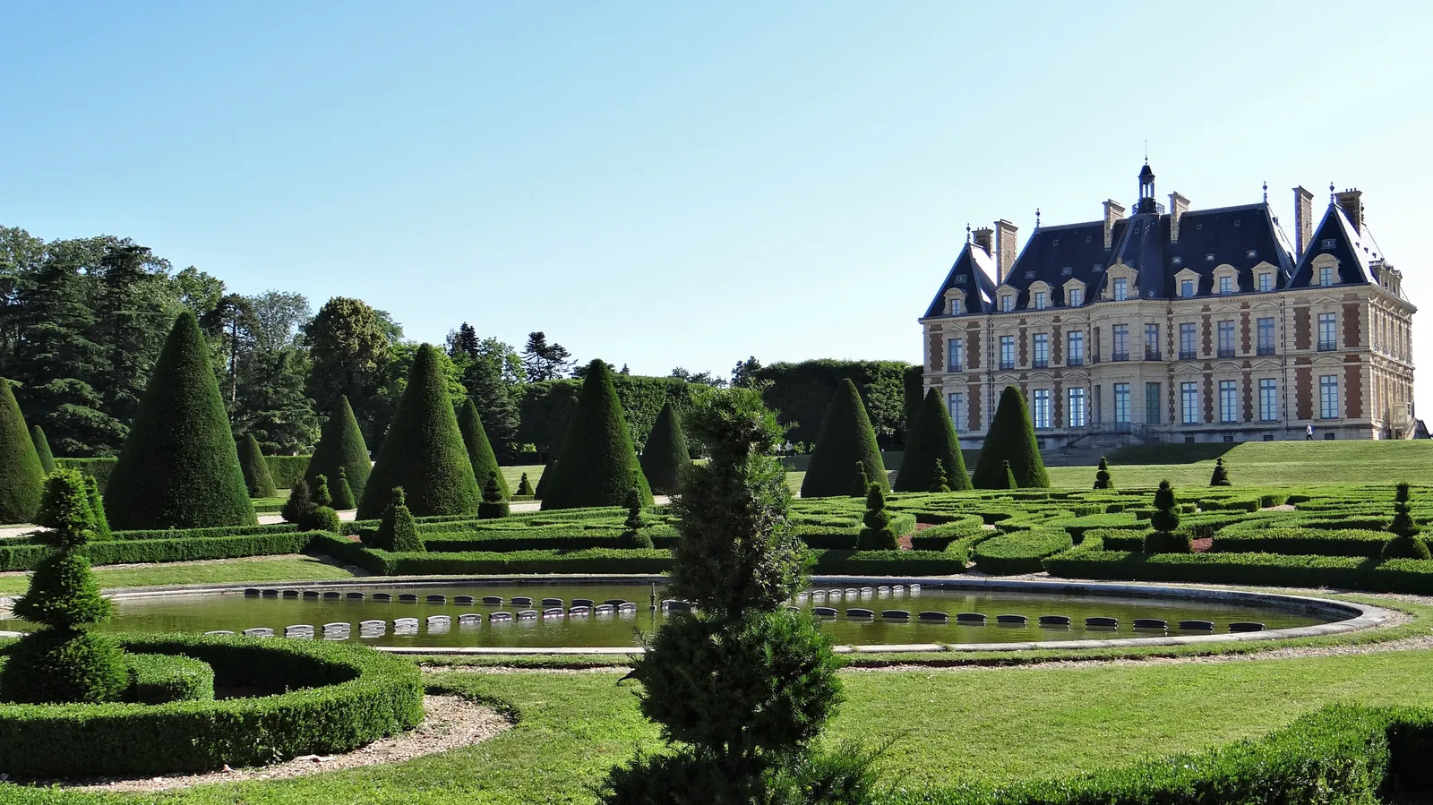 The Château de Sceaux rising behind manicured formal gardens with cone-shaped topiary and a circular pond