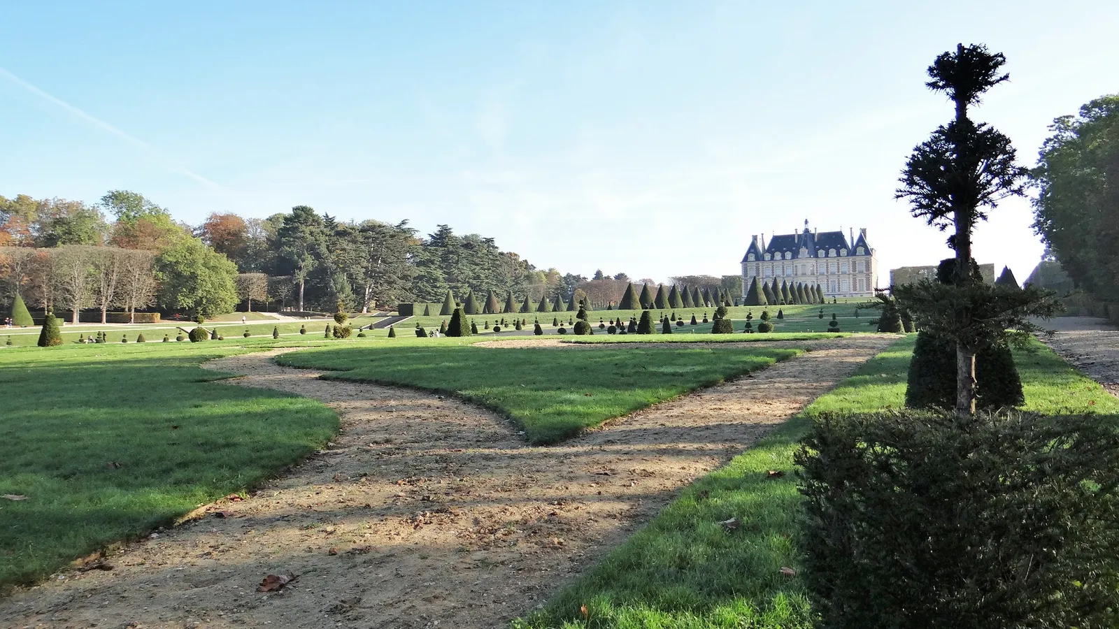 A wide lawn with gravel paths leading toward the Château de Sceaux, lined with tall trees and topiary