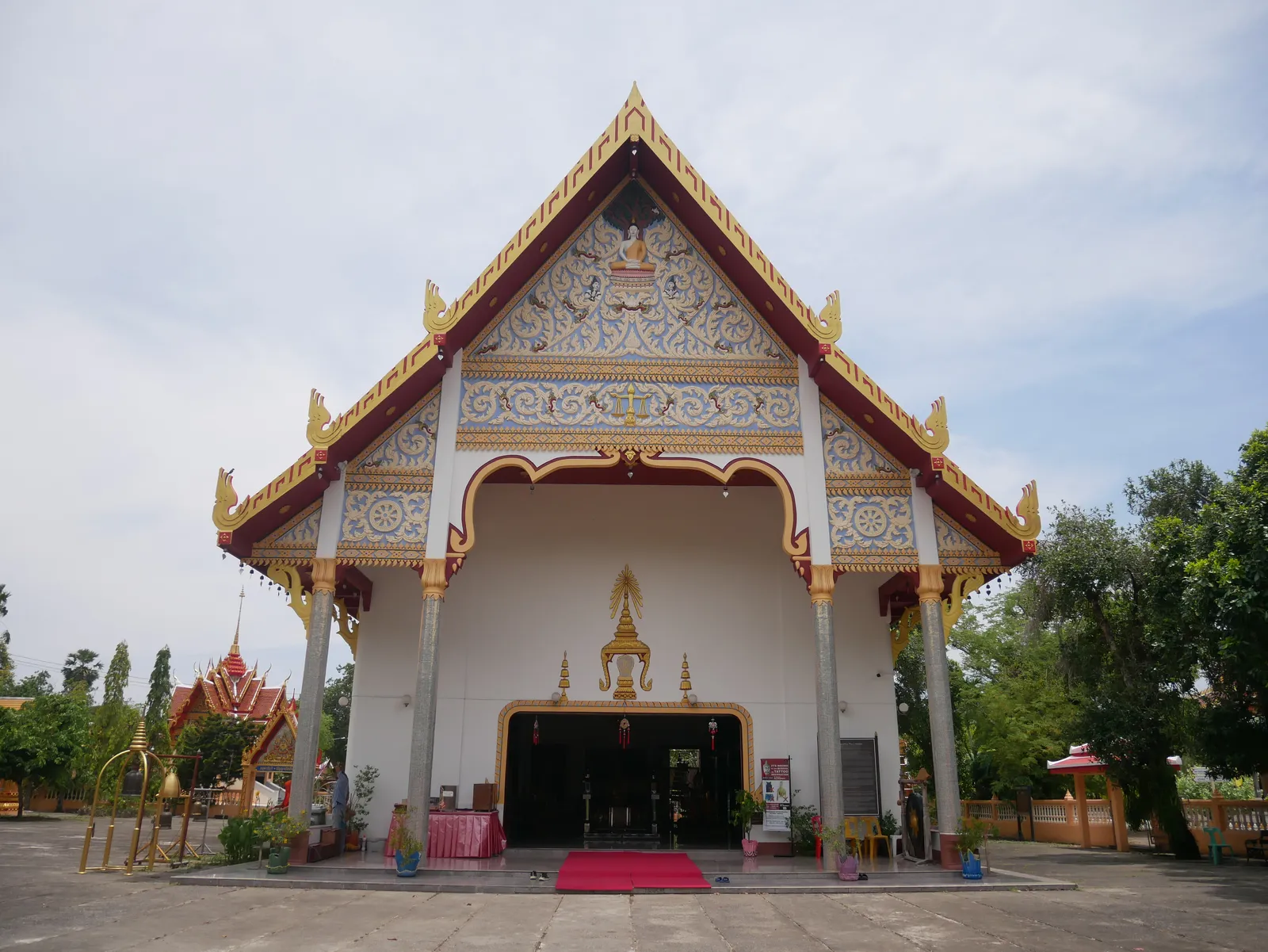 The main hall of Wat Phra Thong in Thalang, Phuket, a white building with a tiered gold-trimmed gable over a dark open doorway and a red carpet running out to the forecourt