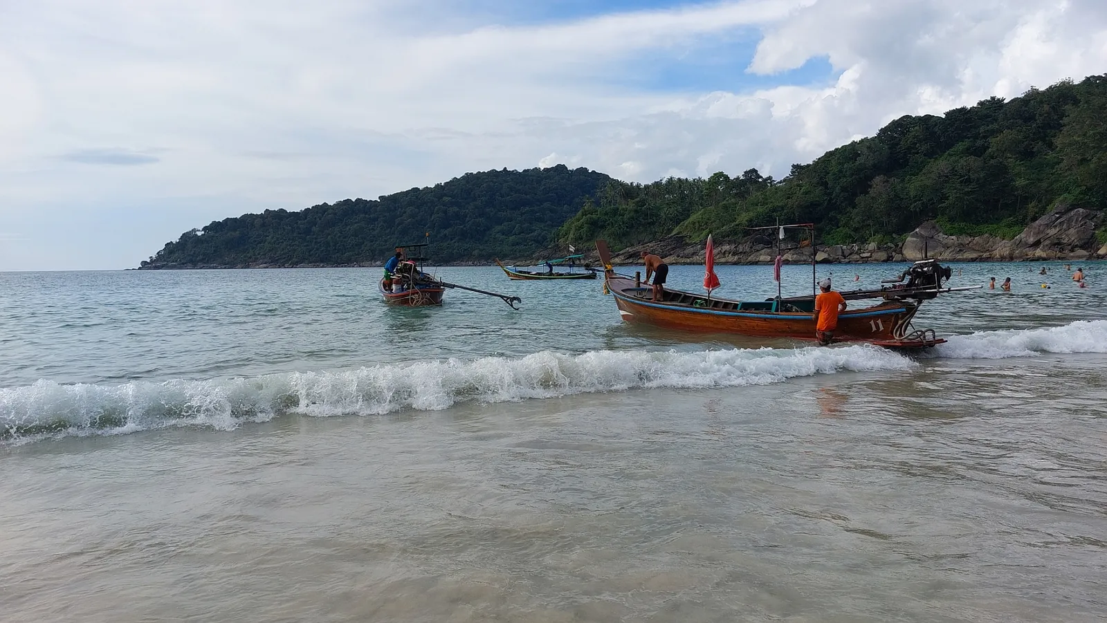 Freedom Beach near Patong in Phuket, two long-tail boats pulled up in the shallows at the edge of a short sandy cove backed by steep jungle-covered slopes