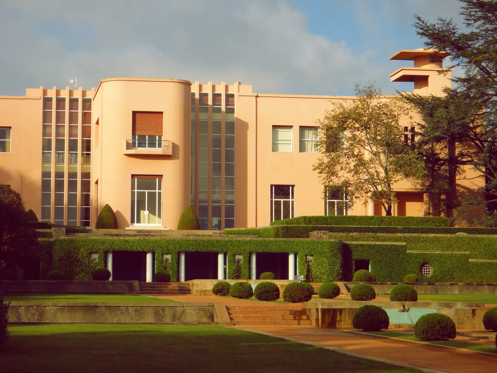 The pink Art Deco front of Casa de Serralves in Porto, with tall strips of windows and clipped hedges on the lawns and terraces in front