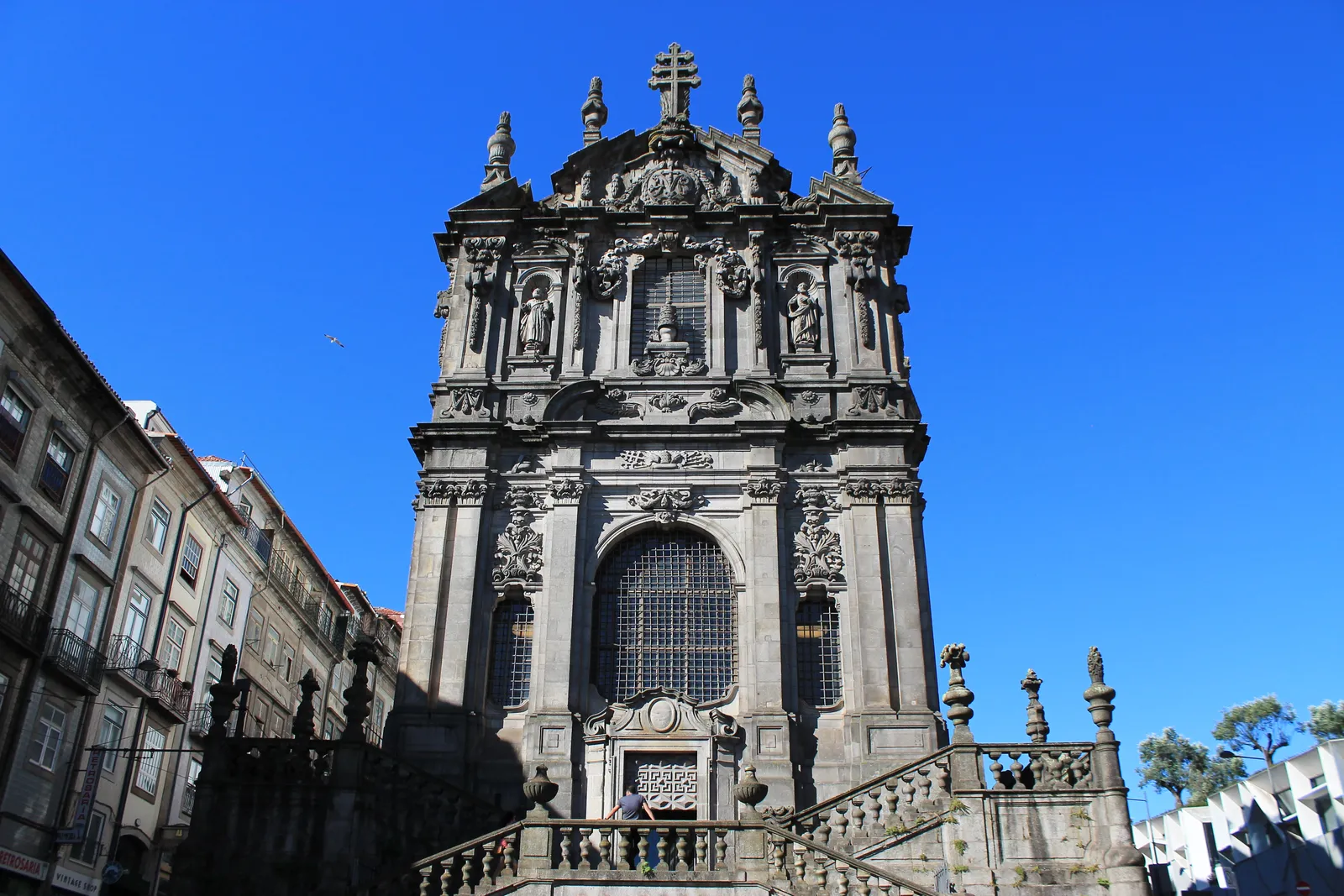 The carved granite baroque facade of the Igreja dos Clérigos in Porto, rising above its curved balustraded staircase against a deep blue sky