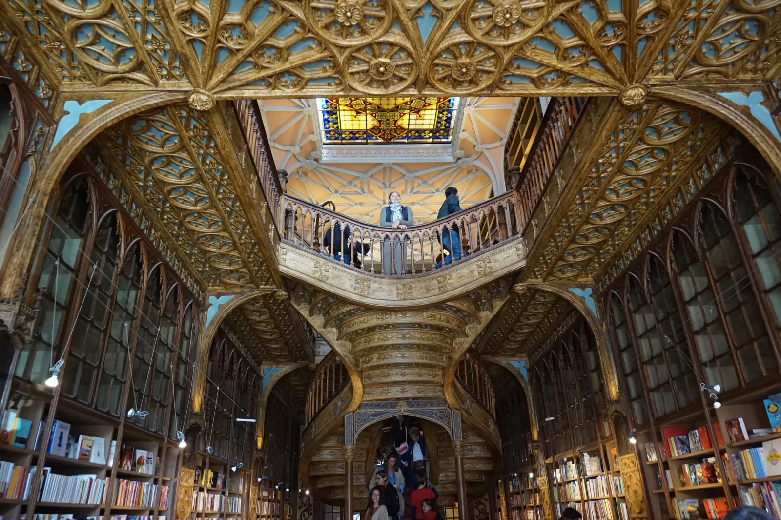 The carved wooden staircase and stained glass skylight inside the Livraria Lello bookshop in Porto, with book-lined galleries on both sides