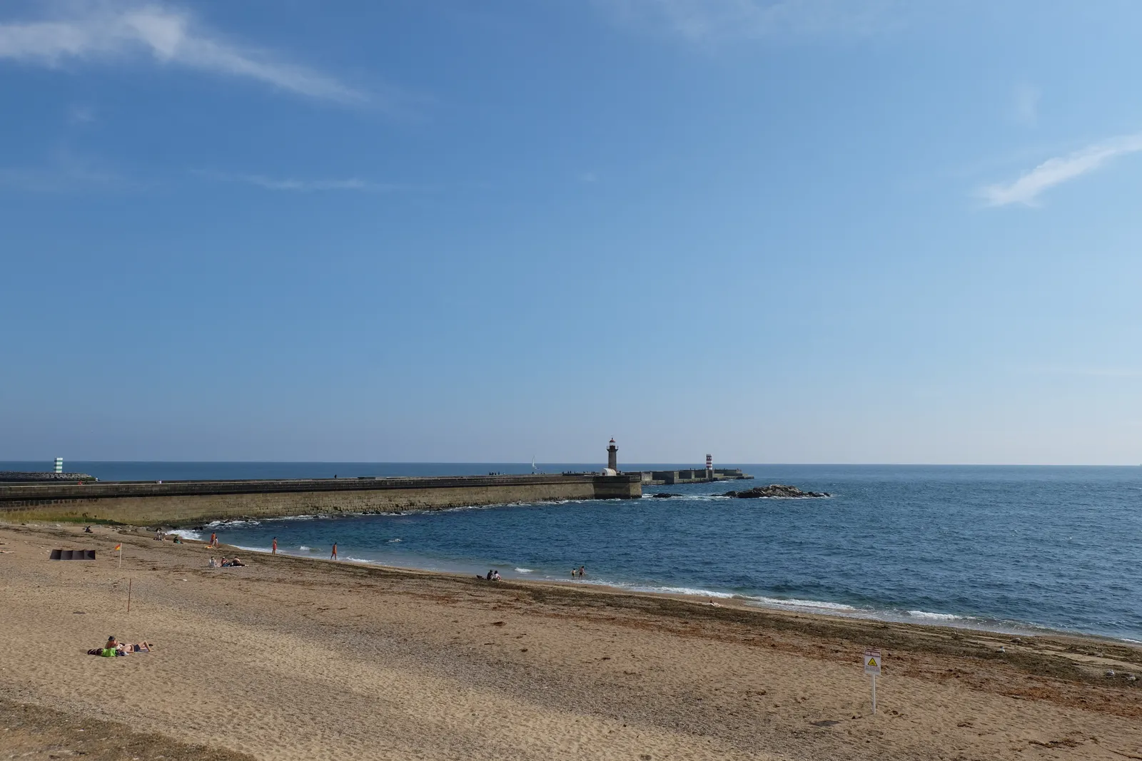 The beach at Foz do Douro in Porto, with the long stone pier and the Felgueiras lighthouse reaching out into the Atlantic under a clear sky
