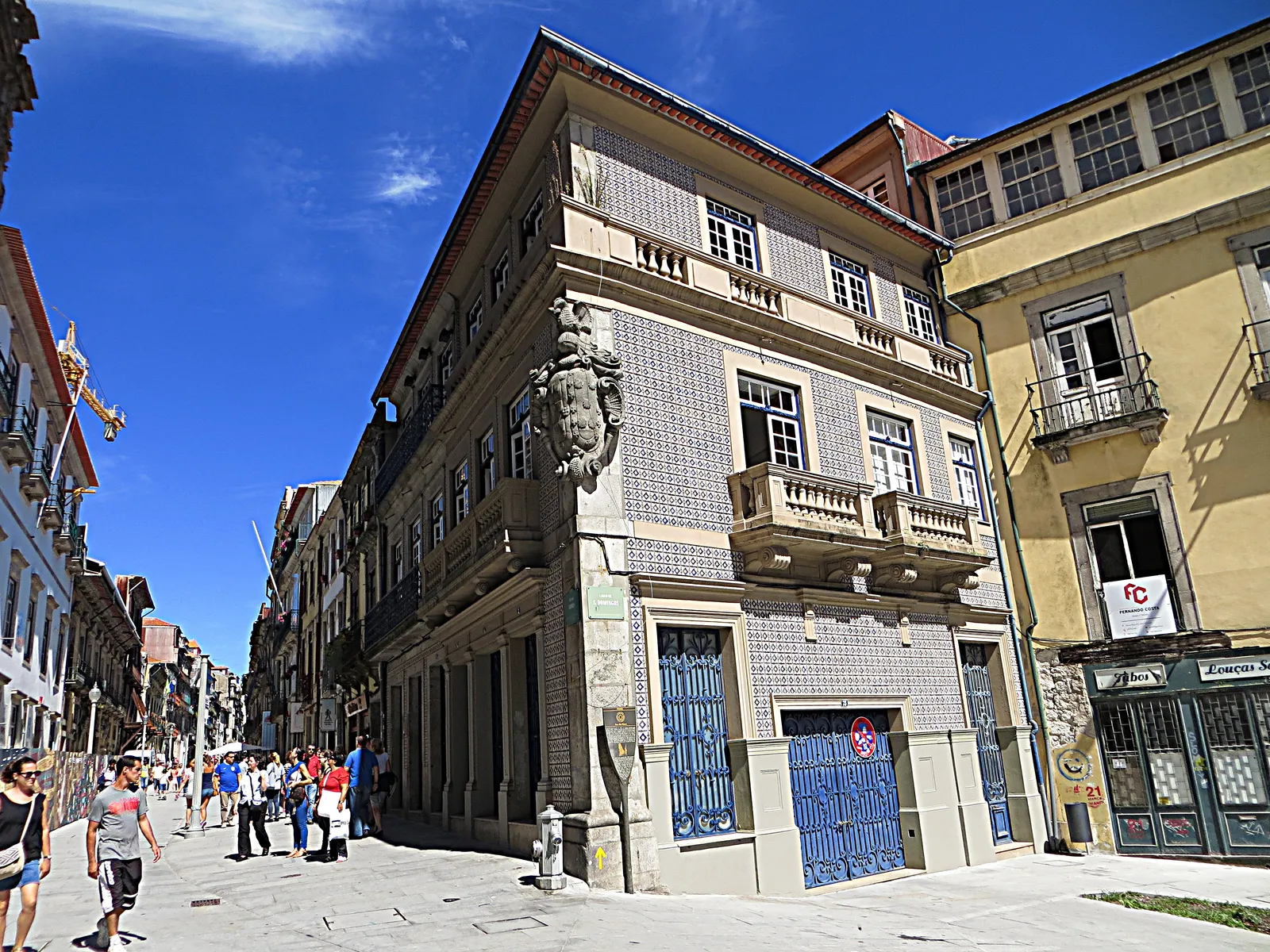 Pedestrians on Rua das Flores in Porto, with a tiled corner townhouse and wrought-iron balconies along the street