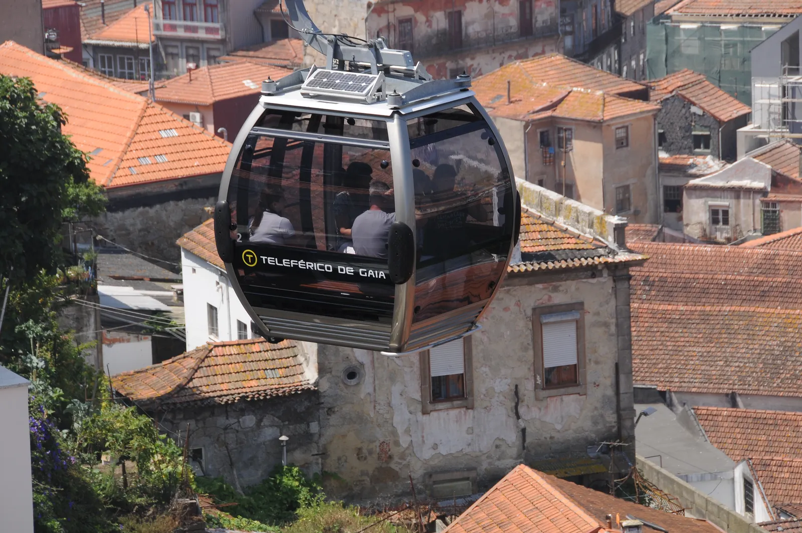 A glass cabin of the Teleférico de Gaia cable car passing above the terracotta rooftops of Vila Nova de Gaia