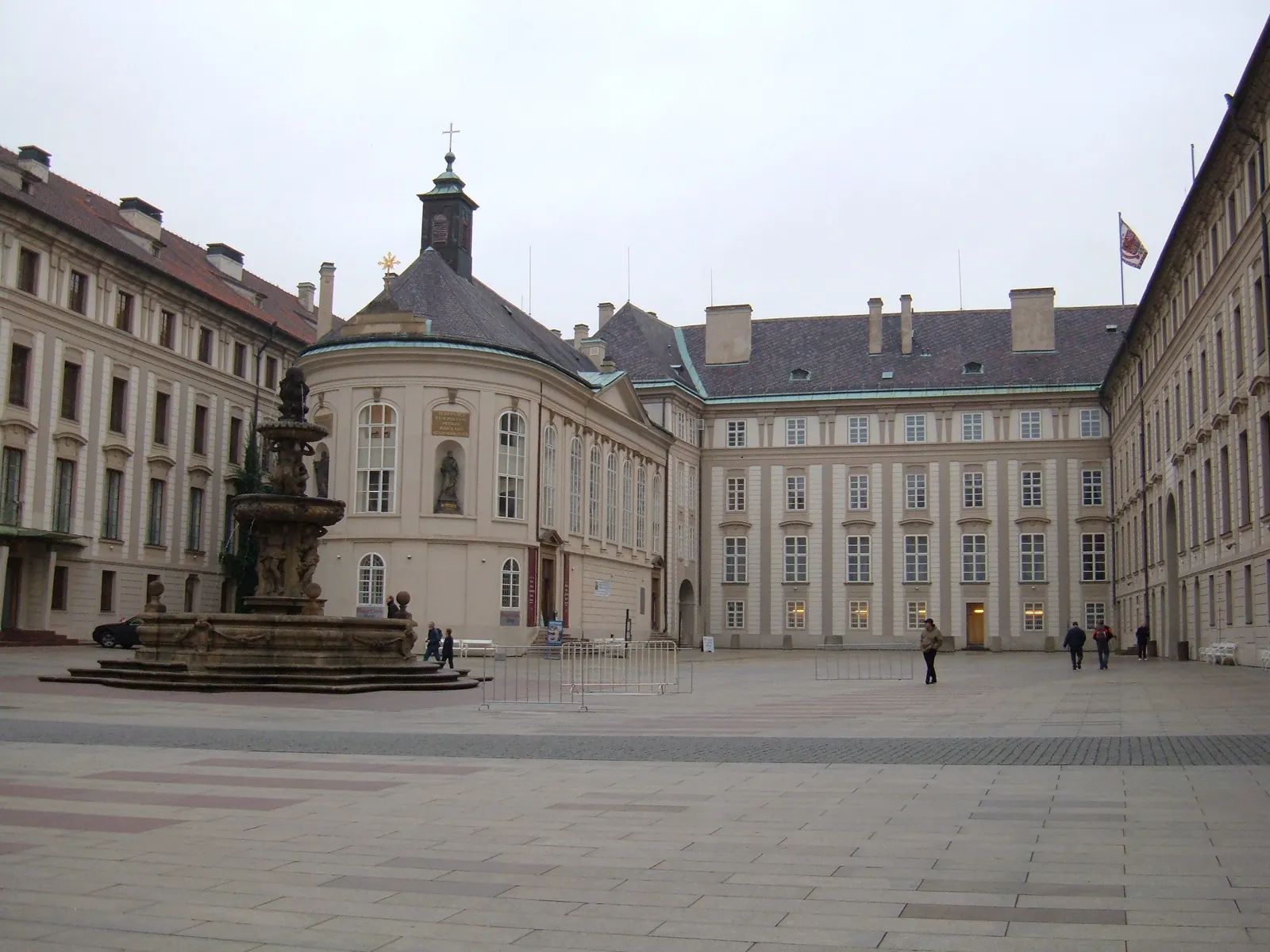 The second courtyard of Prague Castle, a wide paved square enclosed by pale palace wings, with the baroque Kohl Fountain and the domed Chapel of the Holy Cross on the left