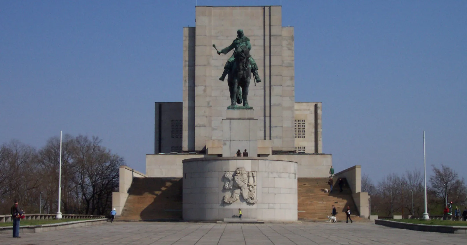 The National Memorial on Vítkov Hill in Prague, a severe grey granite block with the dark bronze equestrian statue of Jan Žižka standing on a plinth in front of it under a clear sky