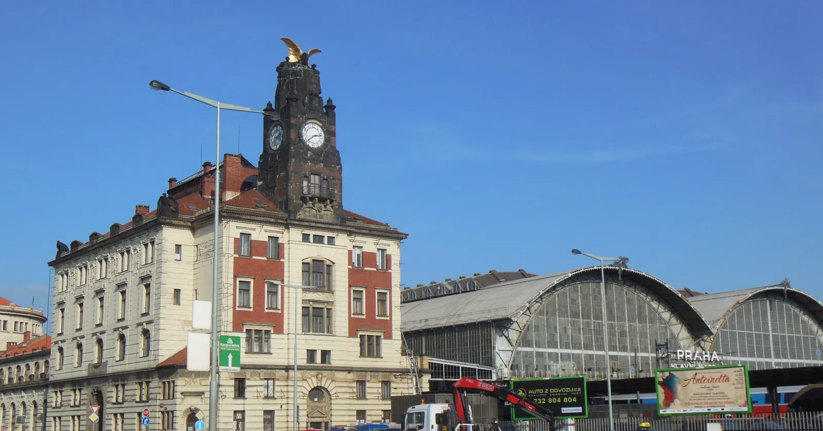 The clock tower of the Fanta building at Prague main station, topped with a gilded winged figure, with the curved glass and steel roof of the platform hall to the right of it