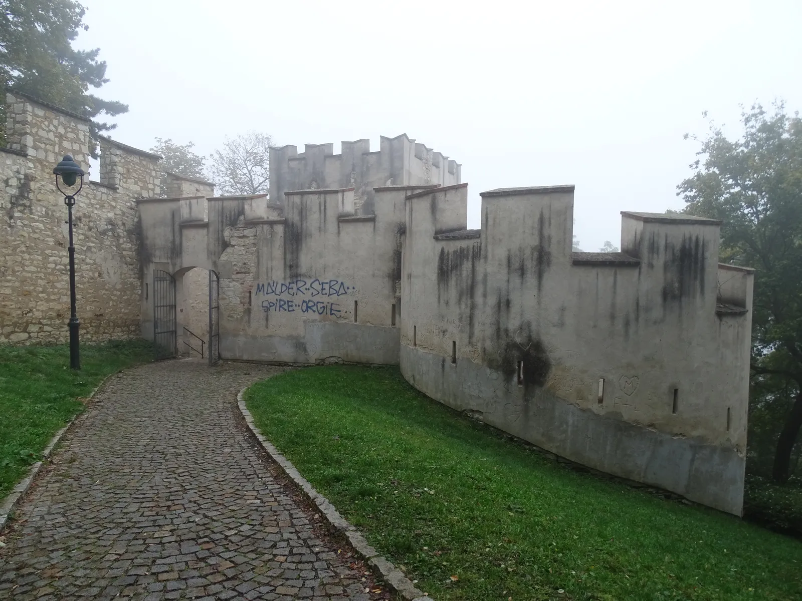 A crenellated section of the medieval Hunger Wall on Petřín Hill with square bastions along it and a cobbled path running through an archway beside it