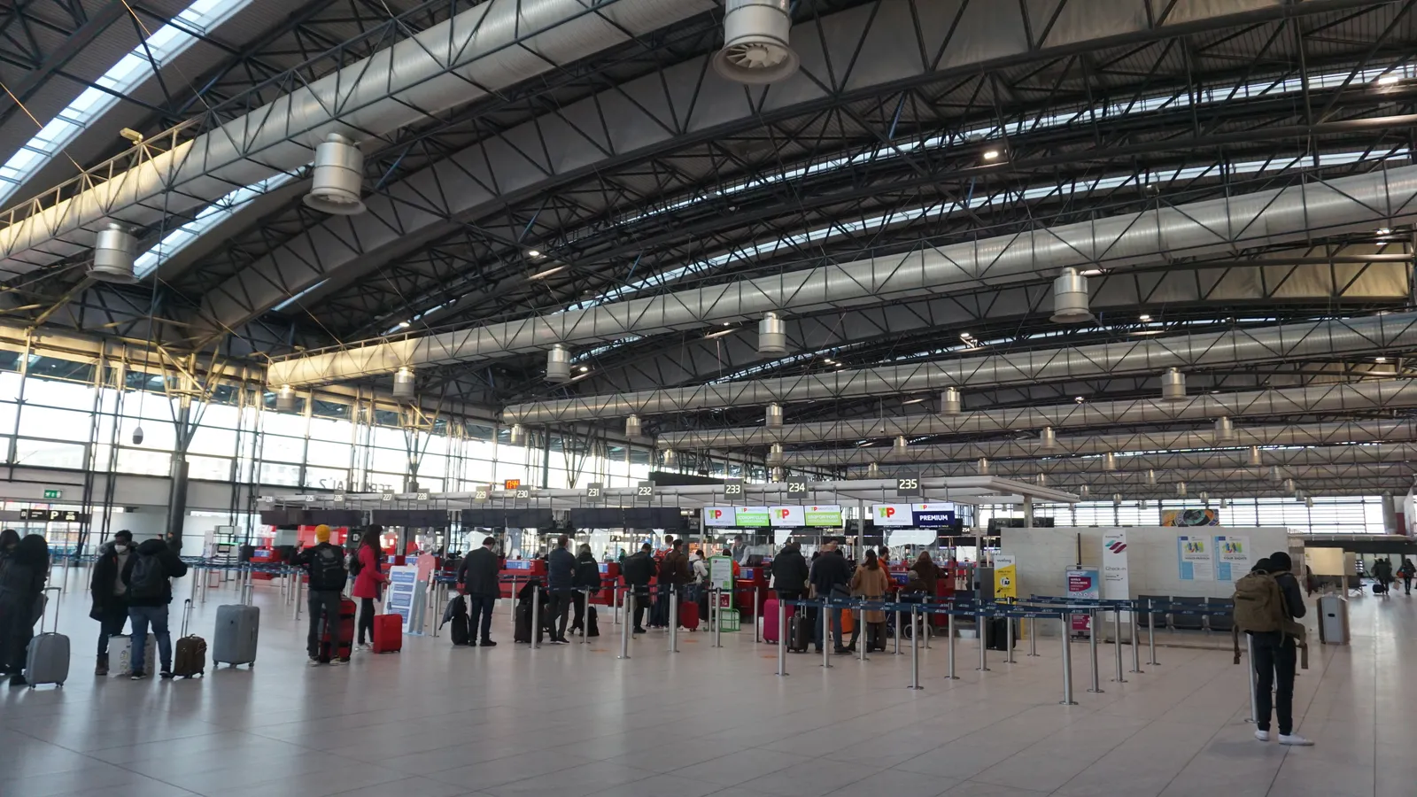 The check-in hall of Terminal 2 at Václav Havel Airport Prague, a wide hall under a curved ribbed roof with rows of check-in desks along the right and passengers queueing with luggage trolleys