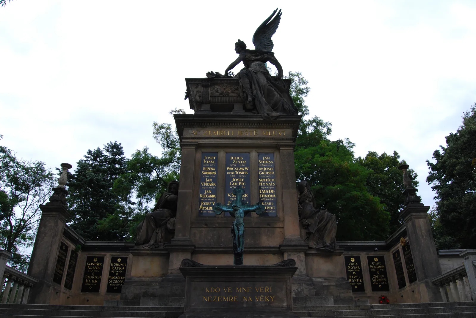 The Slavín tomb in Vyšehrad Cemetery, a stone monument topped by a winged figure, with a bronze crucifix below and panels of engraved names on either side