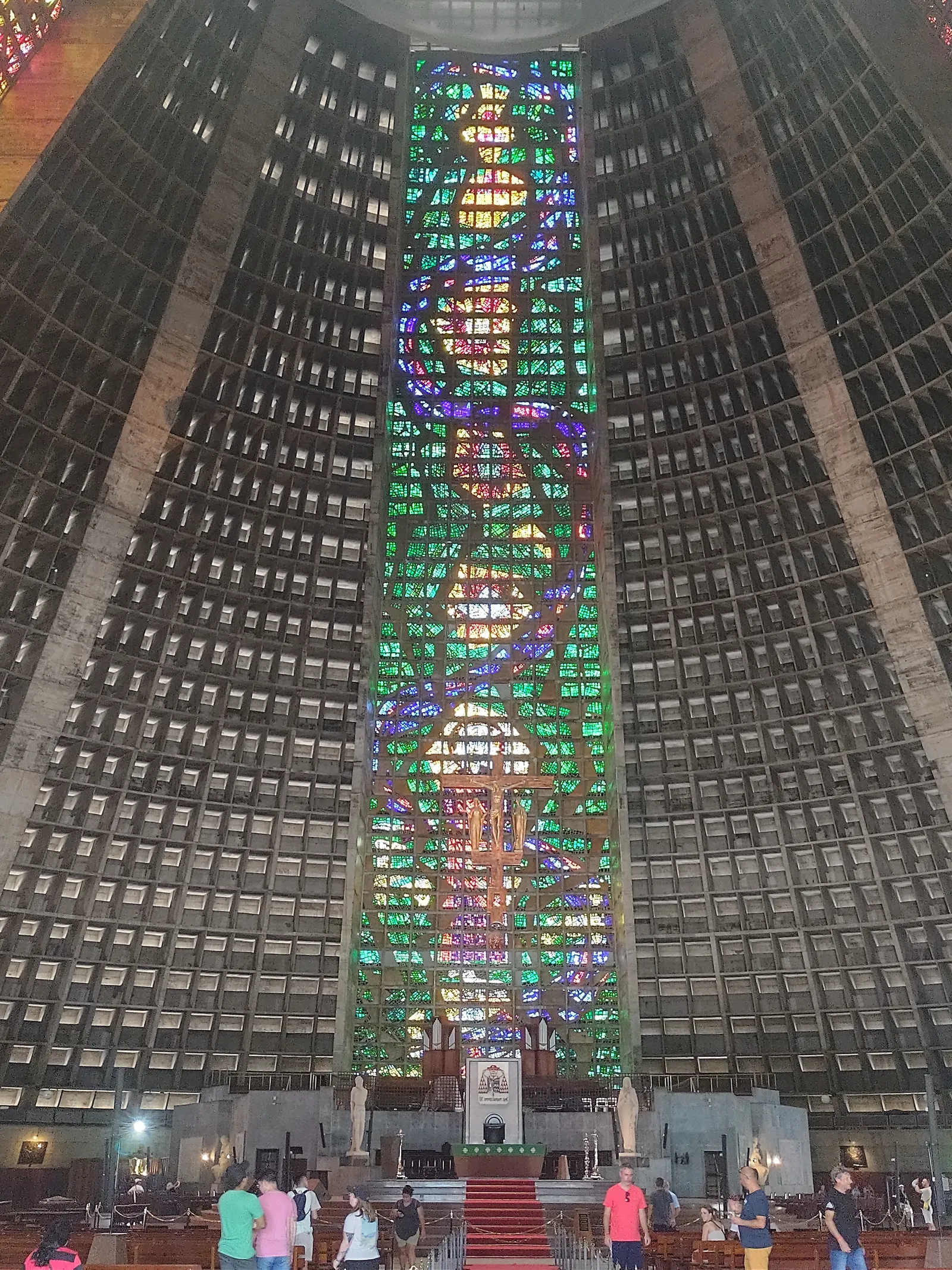 Inside the Metropolitan Cathedral in Rio de Janeiro, a vast cone of ribbed concrete with a single stained-glass strip running the full height of the wall from floor to ceiling and people standing small at the altar below