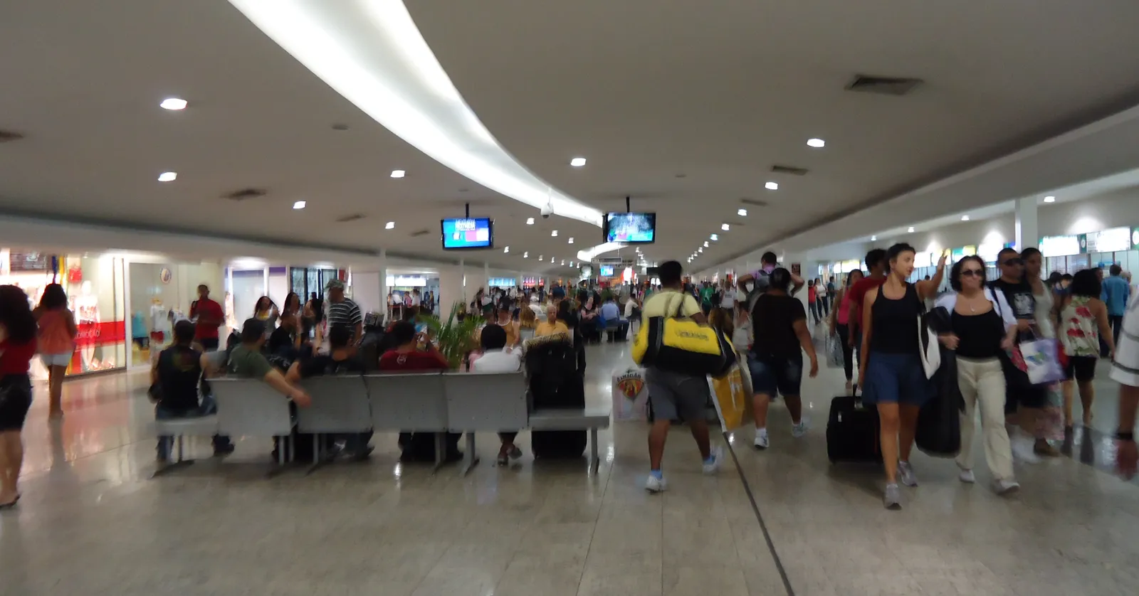 The concourse inside the Novo Rio coach terminal in Rio de Janeiro, a wide low-ceilinged hall with departure screens overhead, rows of seats along one side and passengers crossing with wheeled suitcases