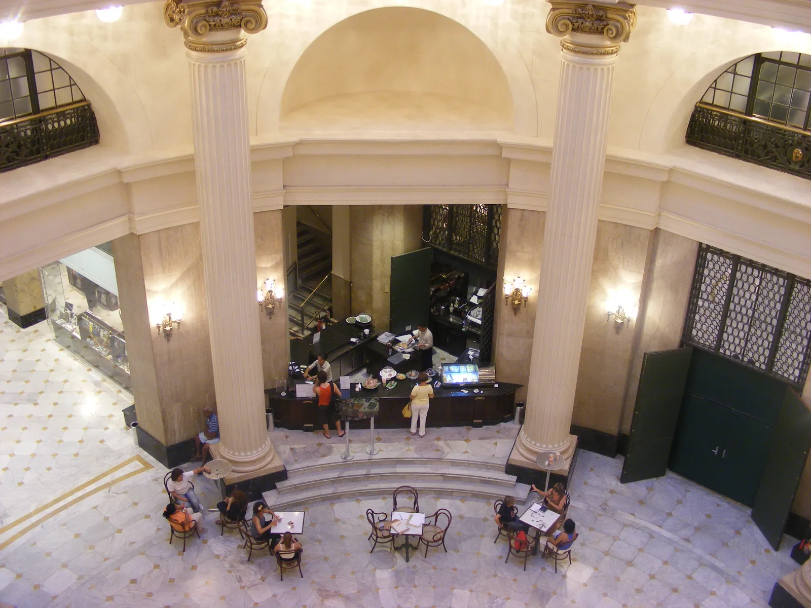 The marble rotunda inside the Banco do Brasil cultural centre in Rio de Janeiro seen from a balcony above, with tall columns, a café counter at the back and small round tables set out on the patterned floor