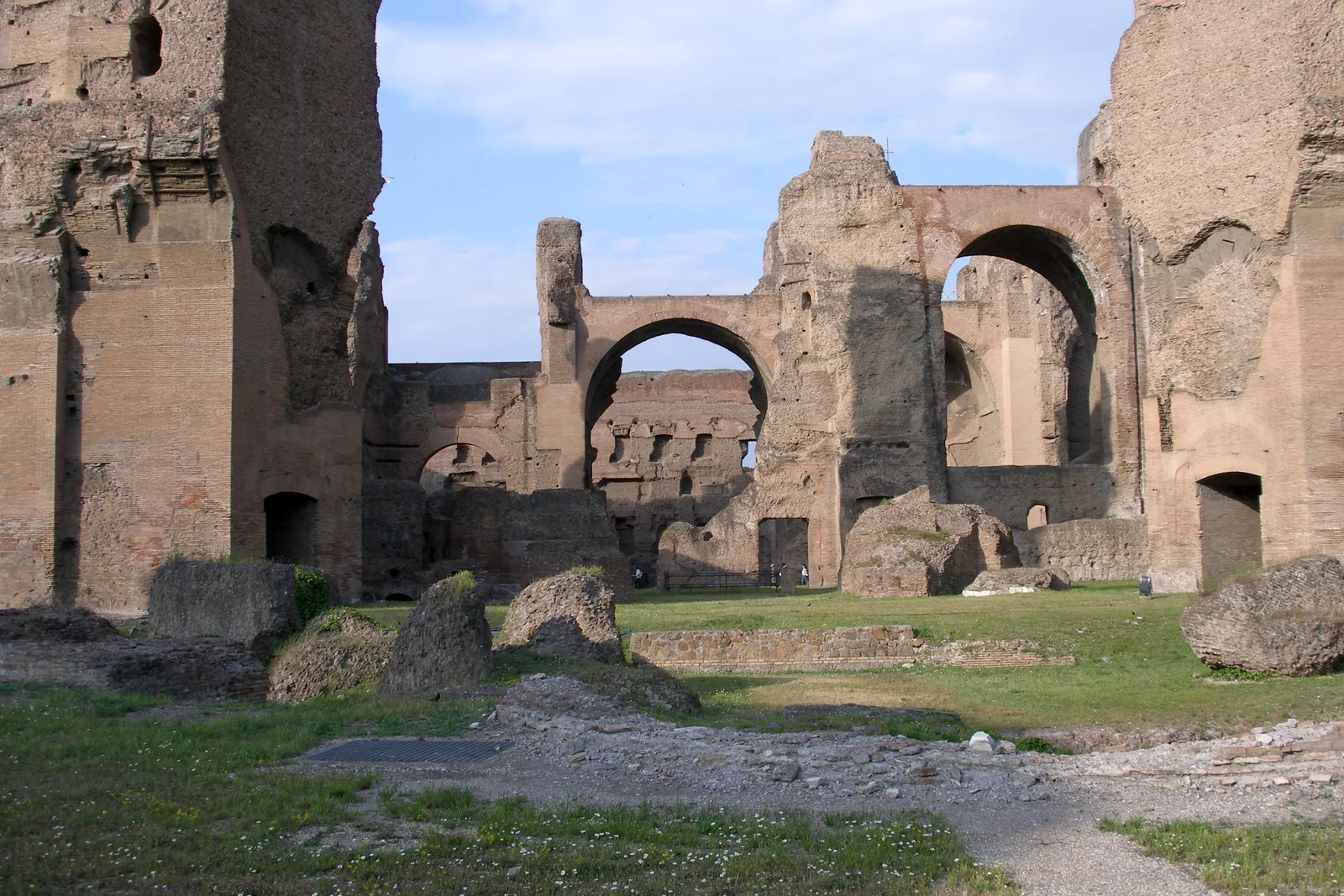 The ancient brick ruins of the Baths of Caracalla in Rome, with towering arched walls and a grass floor