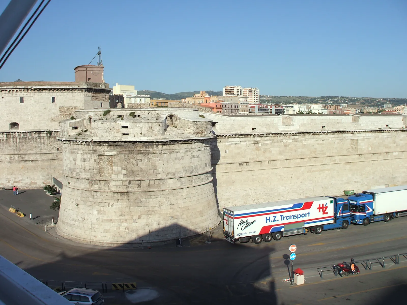 The round stone corner tower and long pale walls of Forte Michelangelo, the sixteenth-century fortress on the harbor at Civitavecchia, with a road and a parked truck below