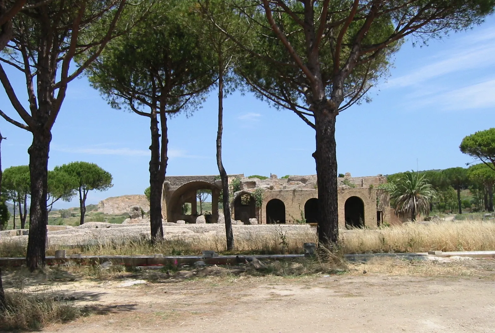 The brick arches of the Roman baths of the Terme Taurine on a hillside above Civitavecchia, framed by umbrella pines on a sunny day