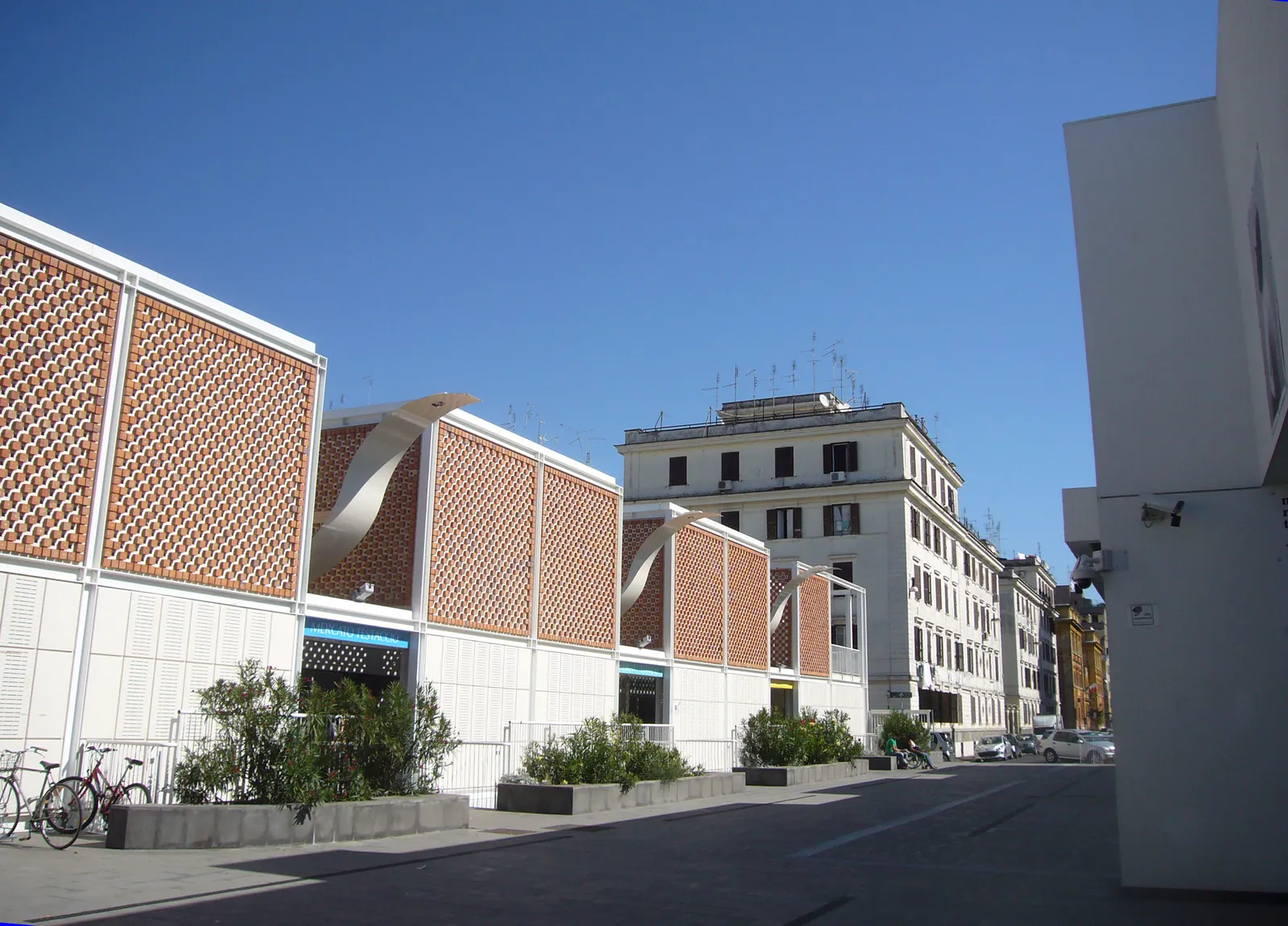 The covered market hall in Testaccio, Rome, a long low building faced in perforated brick latticework with white canopies over its entrances, seen from the street with apartment blocks behind