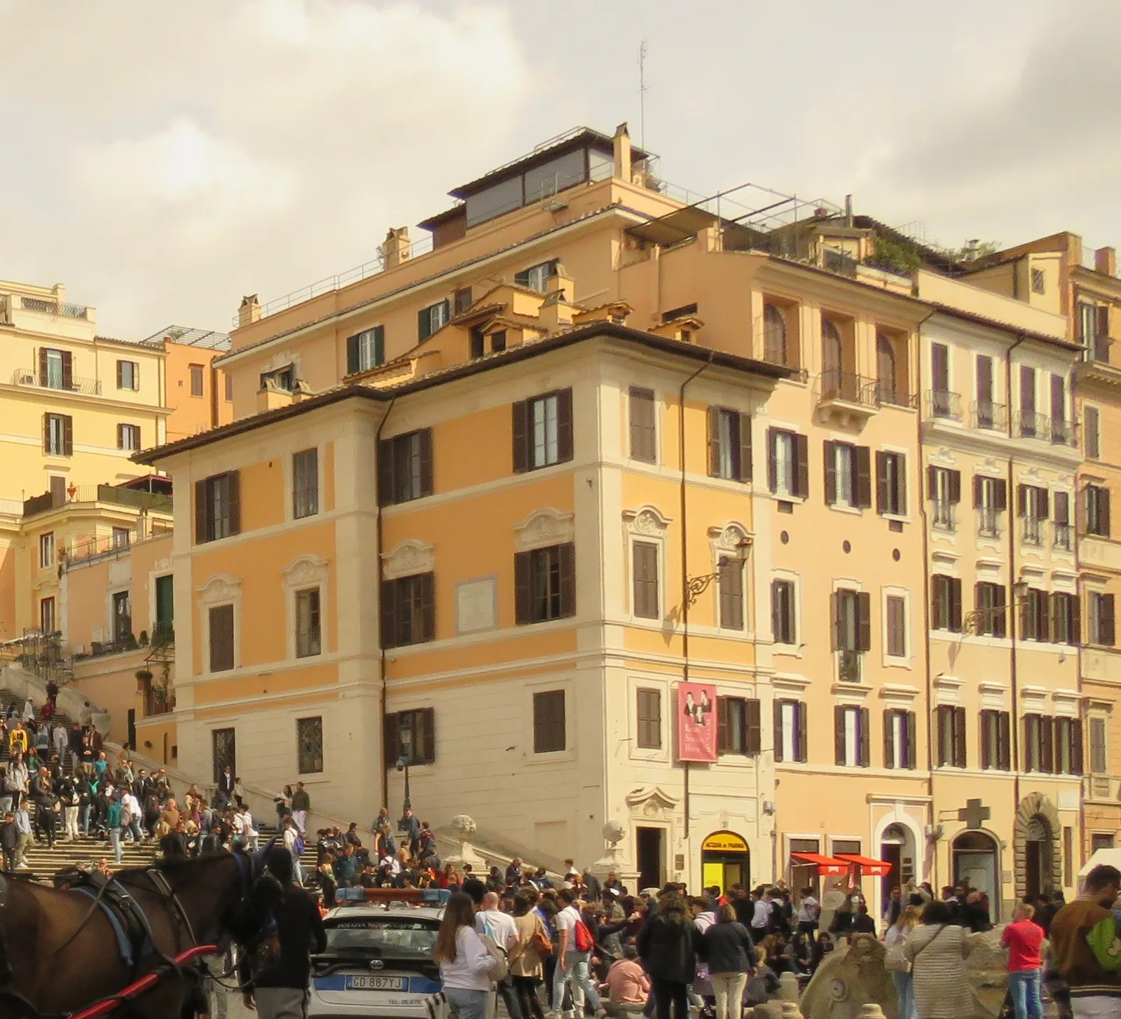 The ochre corner house at the foot of the Spanish Steps in Rome, shuttered windows above a busy square with the bottom of the staircase visible to the left