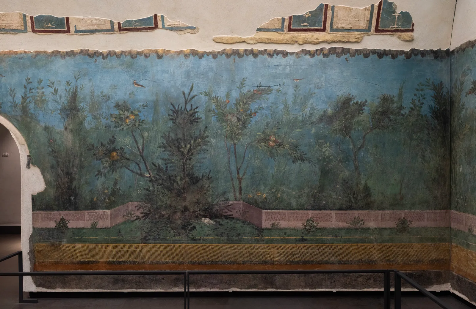 The painted garden wall from the Villa of Livia reassembled at Palazzo Massimo in Rome, a continuous fresco of fruit trees, shrubs and birds against a blue-green sky behind a low painted fence