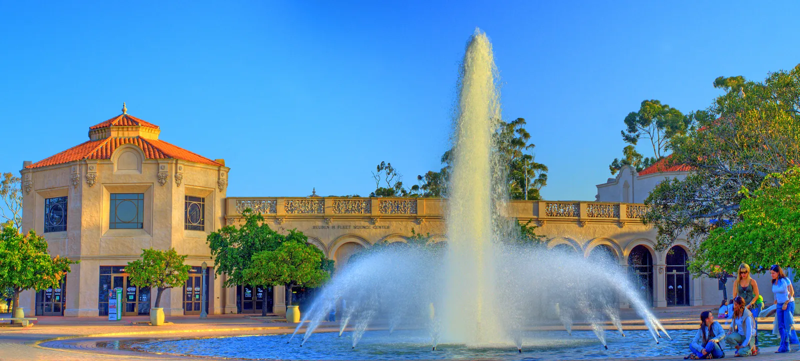The Fleet Science Center in Balboa Park behind the Bea Evenson Fountain, its water thrown high above the plaza in front of the building's tiled dome