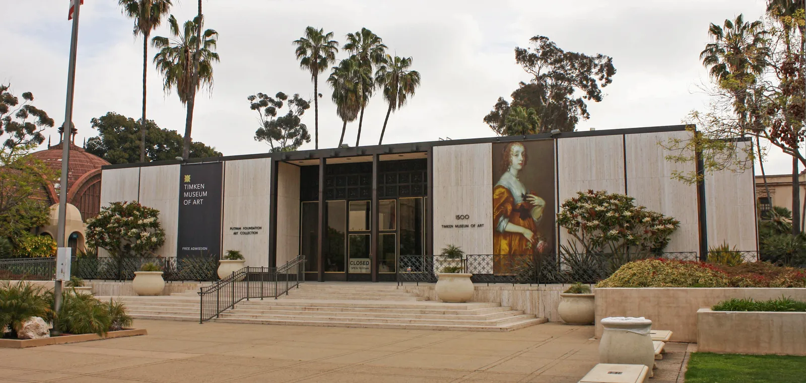 The low modern front of the Timken Museum of Art on El Prado in Balboa Park, with a painted banner between its stone panels and palms rising behind the roof