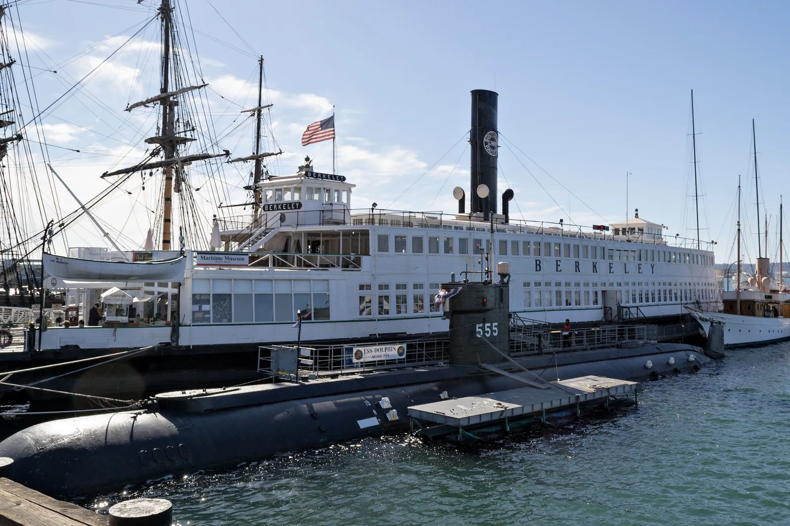 The white steam ferry Berkeley, with its tall black funnel, moored at the Maritime Museum of San Diego, with the dark hull of the submarine Dolphin, number 555, alongside in front
