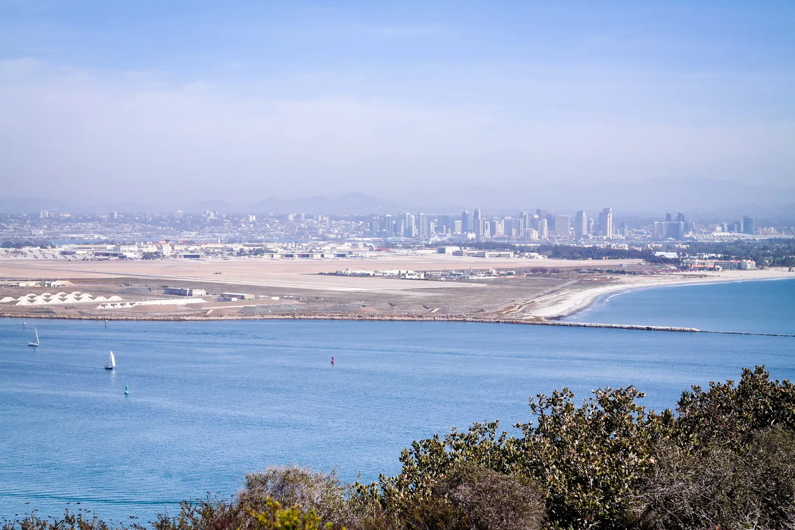 The view from Cabrillo National Monument on Point Loma across the entrance to San Diego Bay, with sailing boats on the water, the naval air station on North Island and the downtown towers in the haze beyond