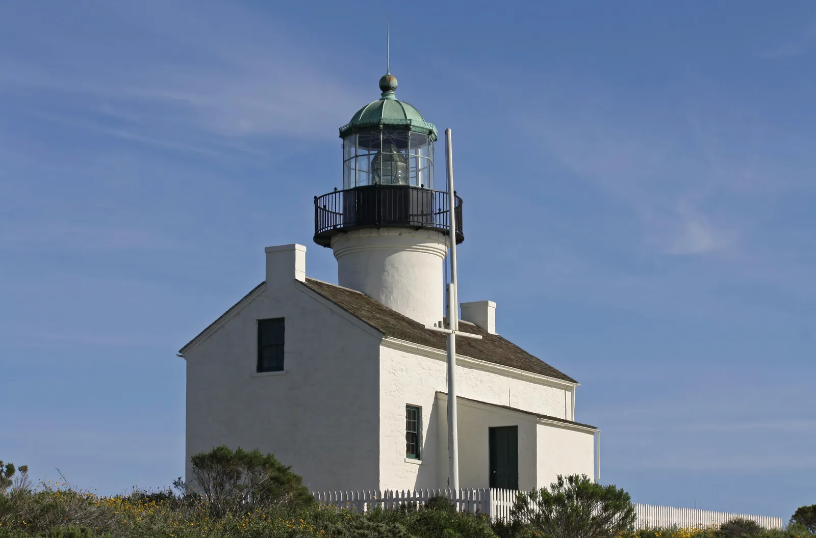 The white Old Point Loma Lighthouse at Cabrillo National Monument in San Diego, a small house with a lantern tower and green dome rising from its roof, against a blue sky