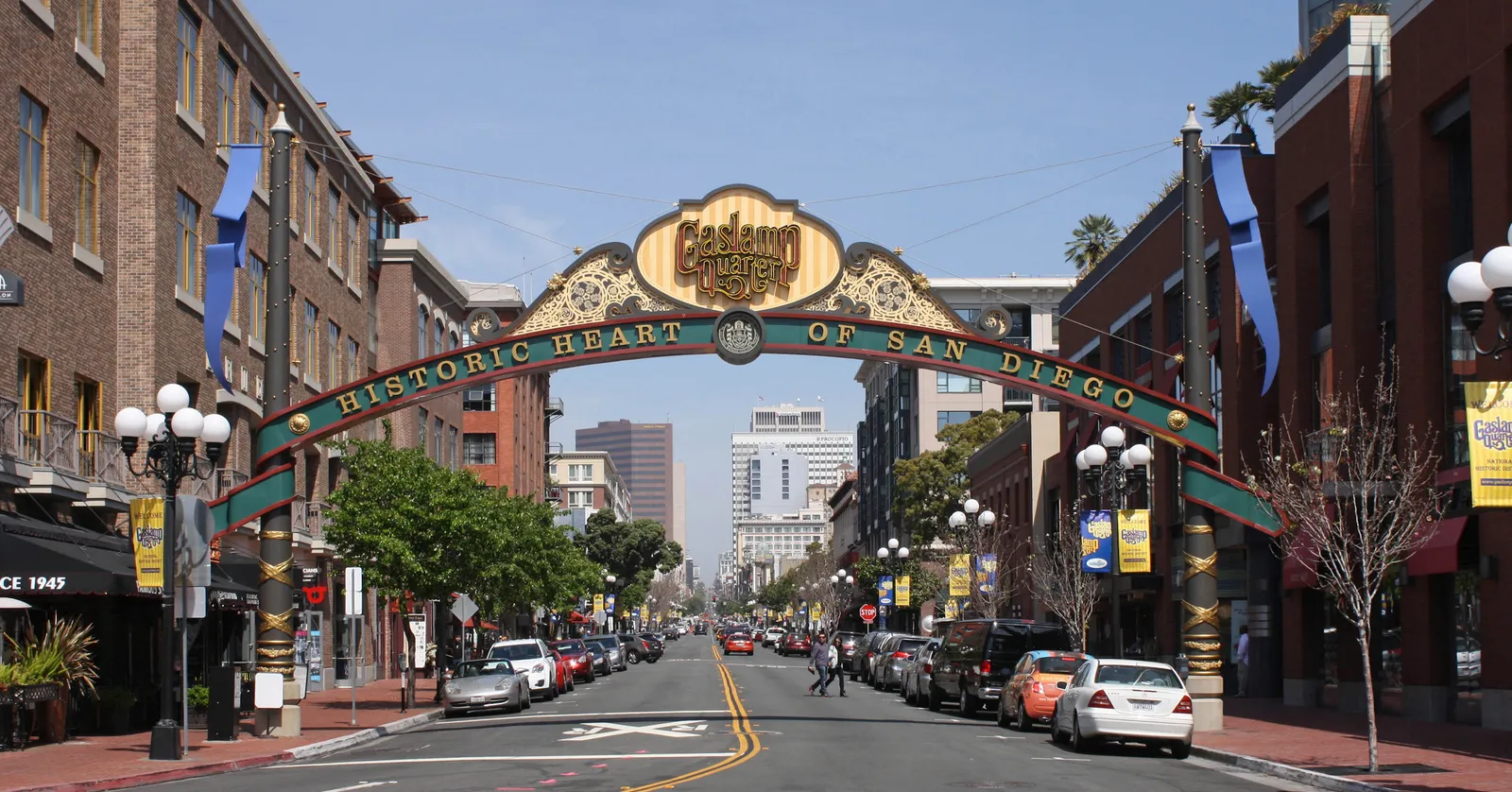 The green and gold Gaslamp Quarter arch spanning Fifth Avenue in San Diego, reading Historic Heart of San Diego, with brick storefronts on both sides and downtown towers beyond