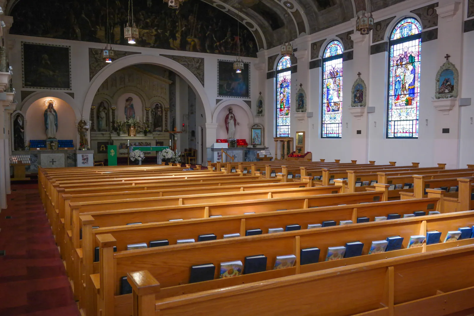 The interior of Our Lady of the Rosary church in San Diego, wooden pews facing a painted sanctuary arch with stained glass windows down the side wall