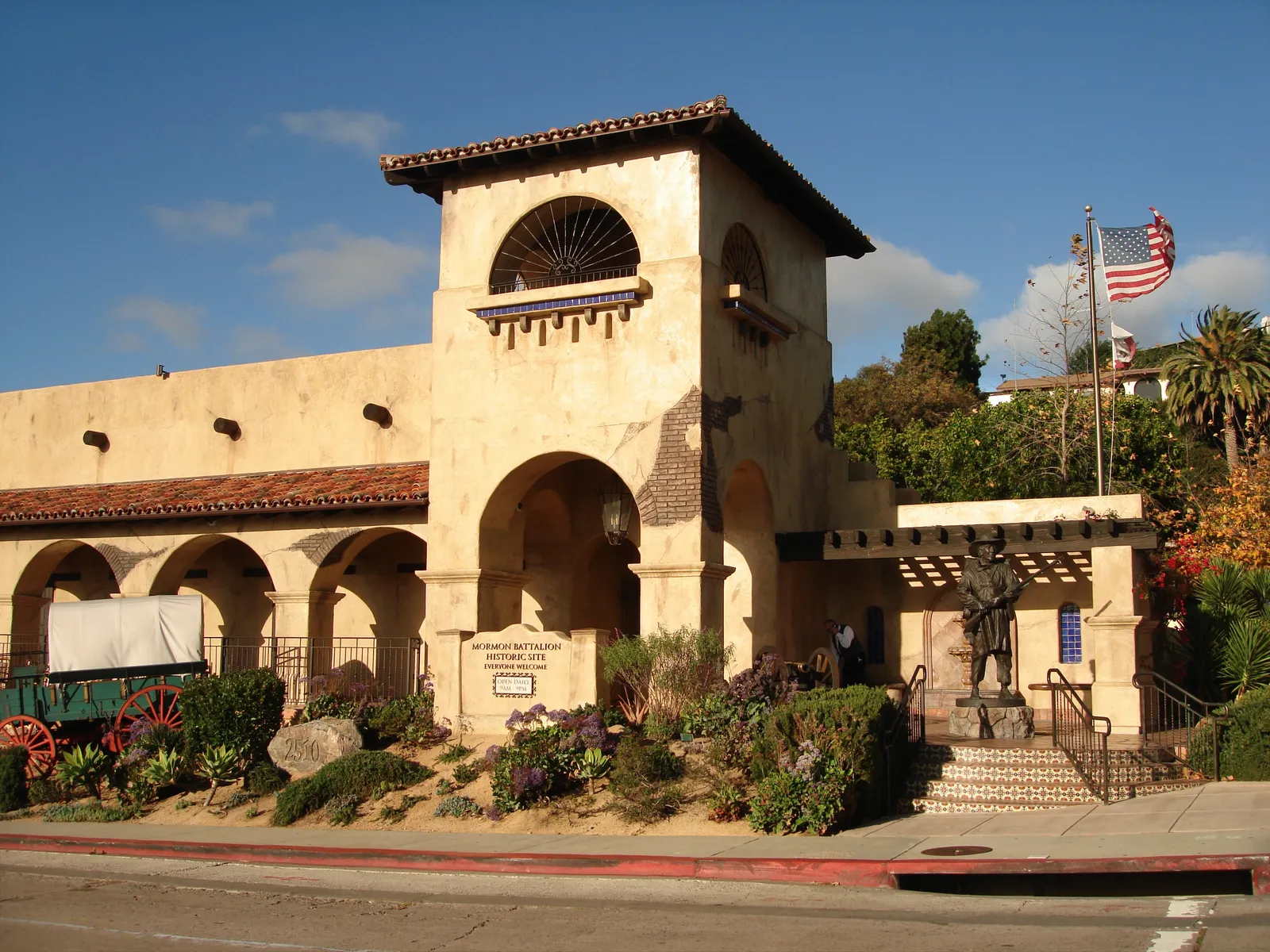 The adobe-colored Mormon Battalion Historic Site building on Juan Street in Old Town San Diego, with an arcaded front, a bell tower and flags flying beside it