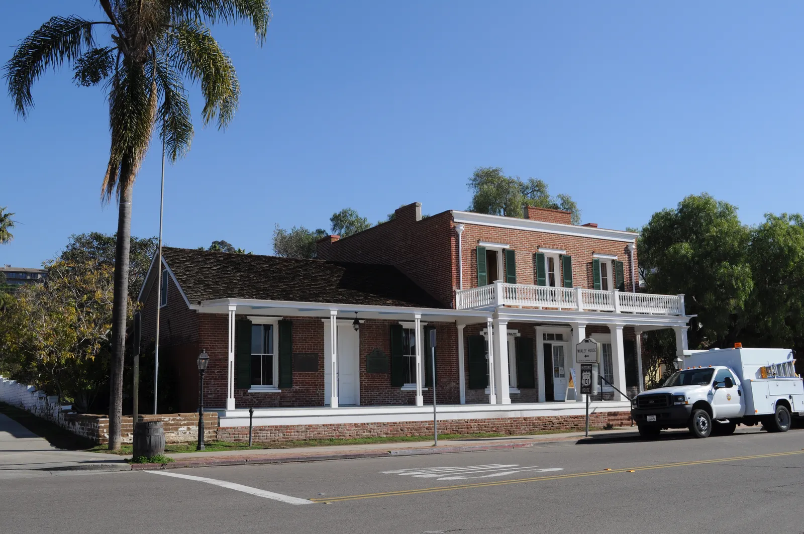 The two-story red brick Whaley House on San Diego Avenue in Old Town, with a white-columned veranda across its front and a palm rising beside it