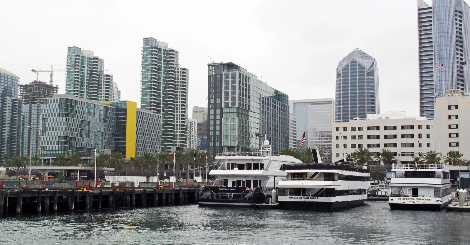 White excursion boats tied up along Broadway Pier on San Diego's Embarcadero, with the downtown high-rises rising directly behind them