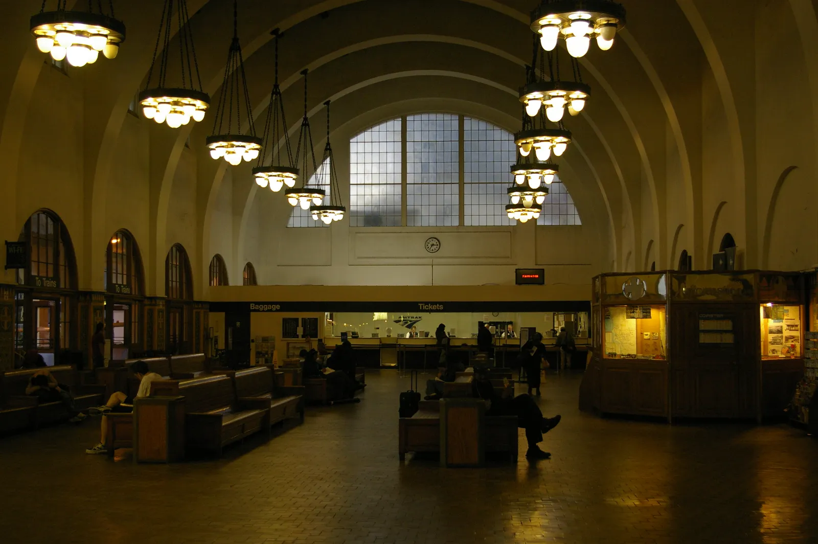 The barrel-vaulted waiting room inside Santa Fe Depot, San Diego, with hanging glass chandeliers, a tall arched window at the far end and wooden benches below
