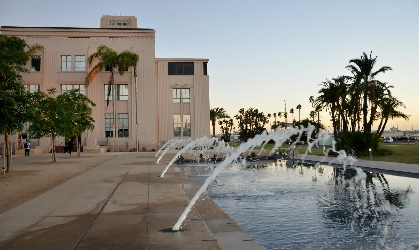 Arcing jets of water in the long fountain at San Diego's Waterfront Park, with the pale San Diego County Administration Center and palms behind it