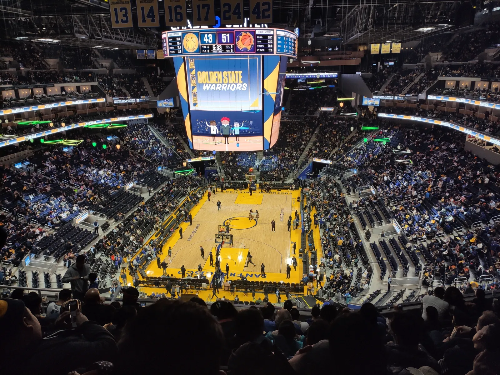 The inside of Chase Center in San Francisco during a Golden State Warriors game, the yellow court below a full bowl of seats with the round scoreboard hanging over centre court