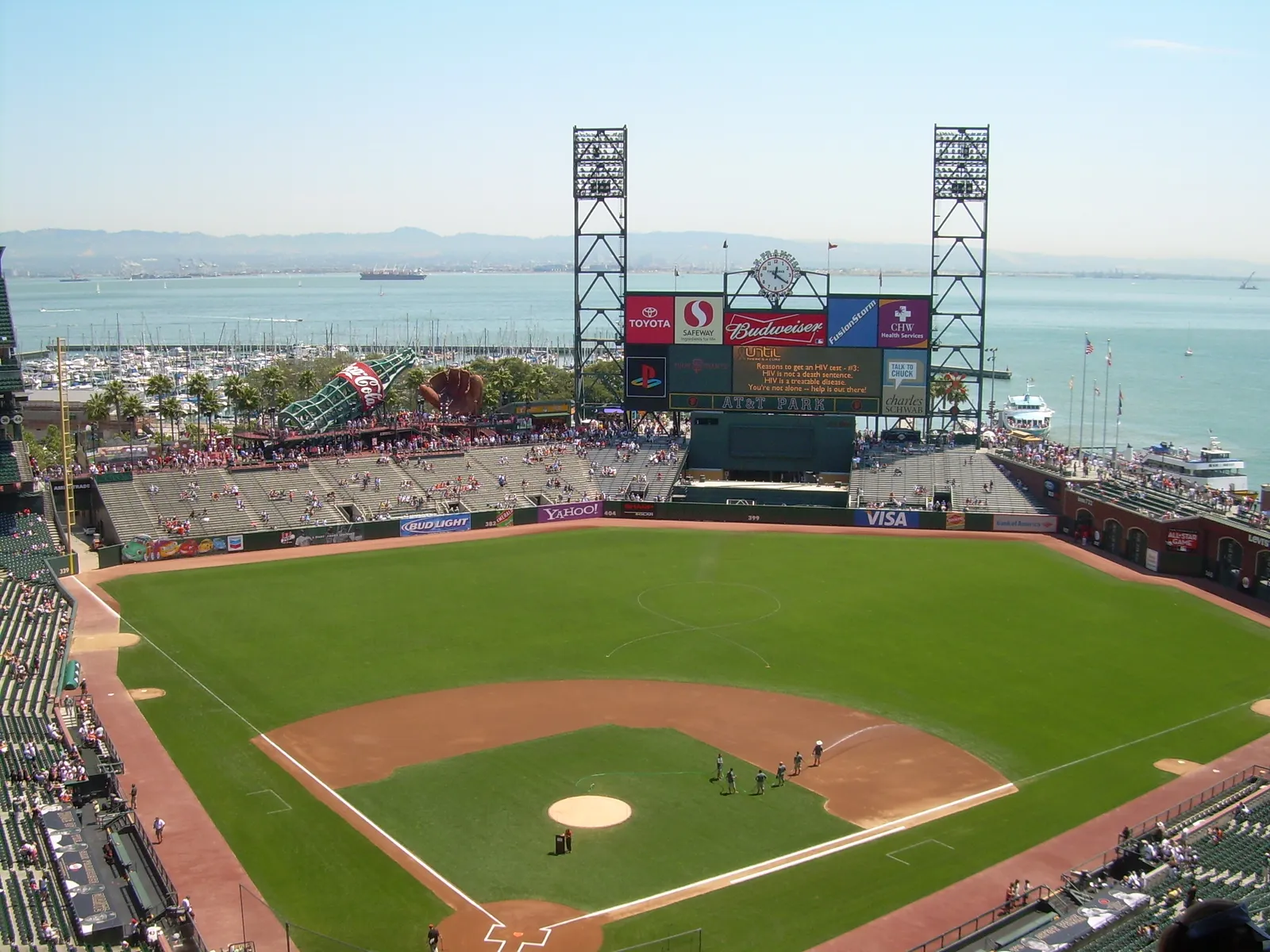 Oracle Park in San Francisco from the upper deck, the infield and outfield laid out below with the scoreboard, the right field arcade and the boats moored in McCovey Cove and the bay beyond