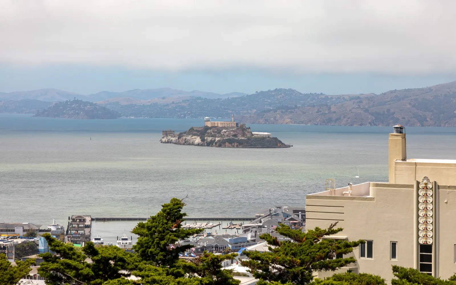 The view north from Pioneer Park on Telegraph Hill in San Francisco, Alcatraz Island sitting low in the grey bay with the Marin hills beyond and the fluted base of Coit Tower at the right edge