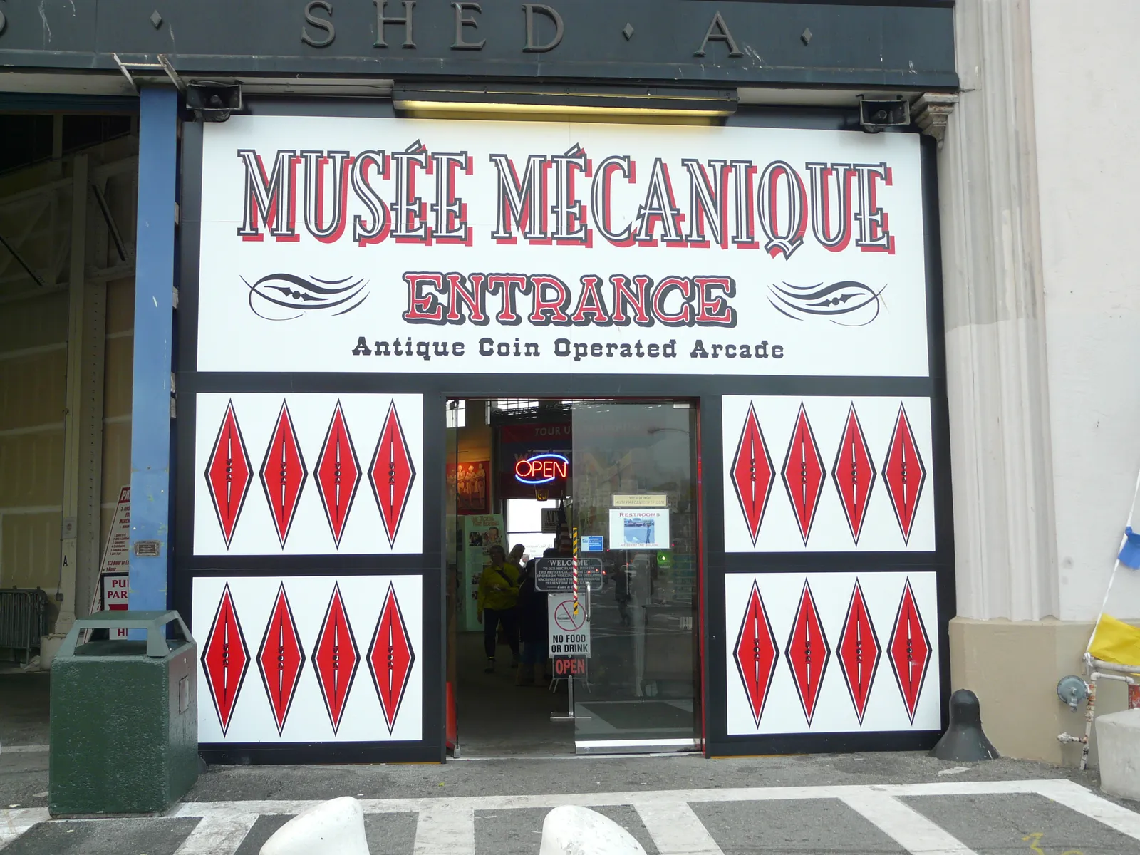 The painted entrance to the Musée Mécanique on Pier 45 in San Francisco, a hand-lettered sign reading Antique Coin Operated Arcade above open glass doors in a warehouse shed