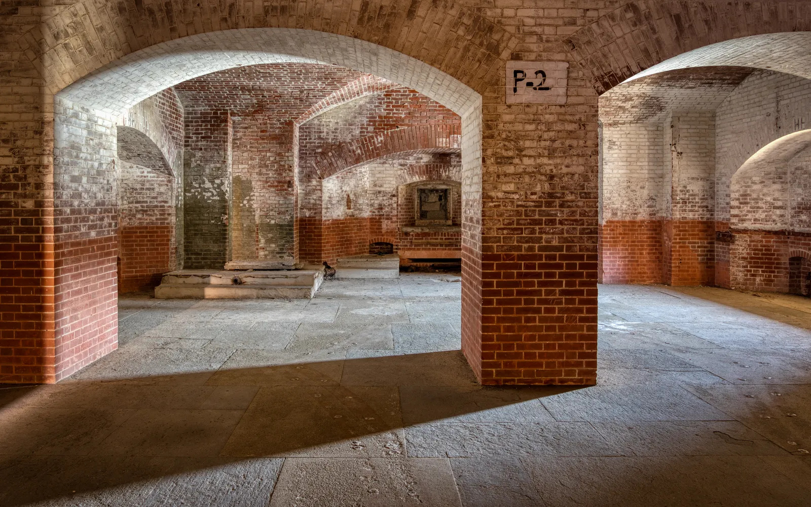 Brick casemates inside Fort Point in San Francisco, rows of low arched openings in red and whitewashed brick over a bare stone floor with daylight falling through one side